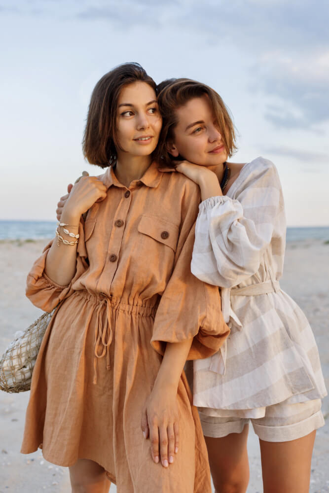 Duas modelos vestindo roupas de linho em cor neutra: uma com vestido e outra com conjunto.