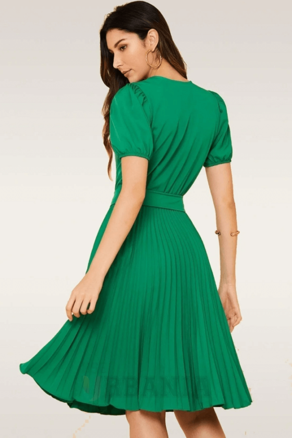 Mulher vestindo vestido plissado verde bandeira, comprimento midi, modelagem rodada, com cinto e mangas estilo princesa.